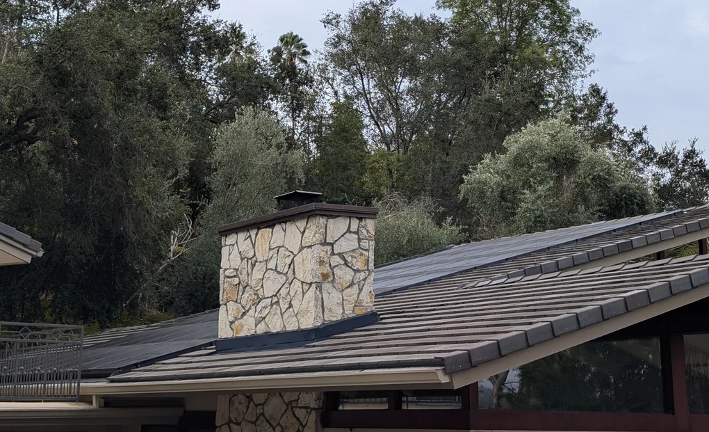 After: new concrete tile roof with the solar panels reinstalled, next to the stone chimney