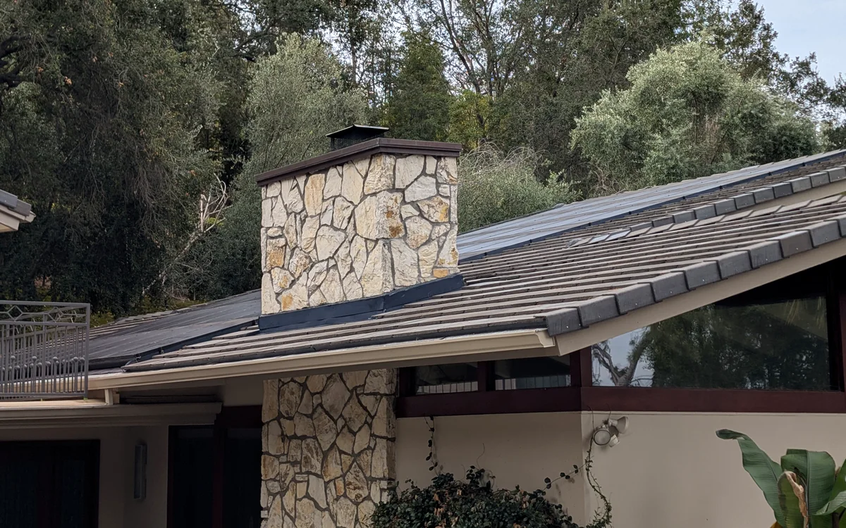 Finished tile roof with solar panels reinstalled beside a stone chimney, a Green Conception RRR job
