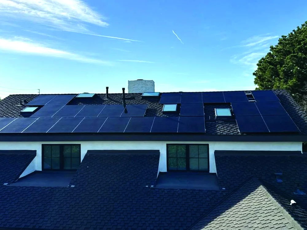 All-black solar panels across the roof of a two-story home under a blue sky, installed by Green Conception